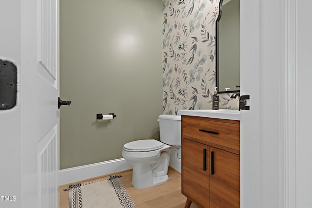 half bath with toilet, baseboards, wood finished floors, and vanity