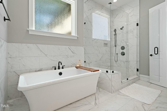 bathroom with a stall shower, marble finish floor, a freestanding bath, and tile walls