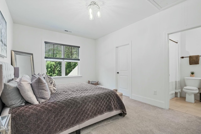 bedroom featuring visible vents, attic access, light carpet, ensuite bath, and baseboards