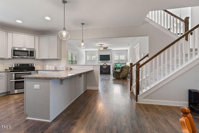 kitchen with light stone counters, dark wood-type flooring, white cabinetry, appliances with stainless steel finishes, and a breakfast bar area