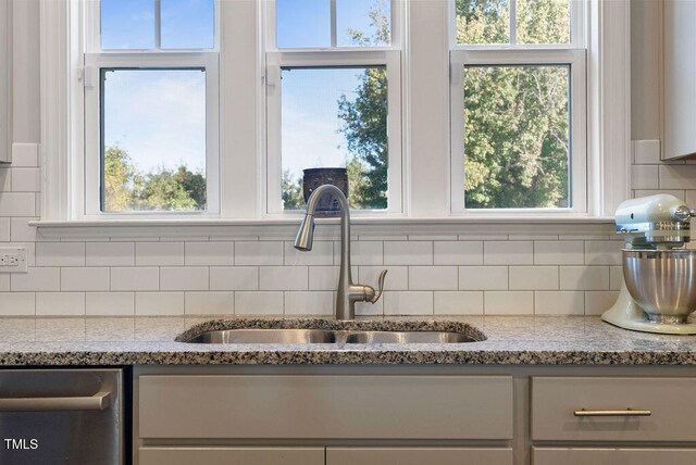 interior details with light stone counters, backsplash, sink, and stainless steel dishwasher