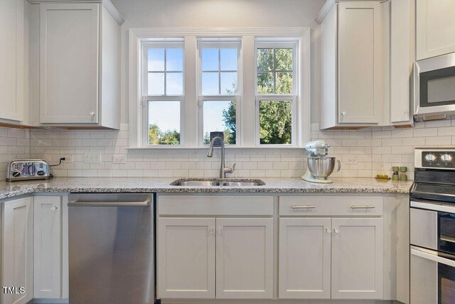 kitchen with decorative backsplash, sink, light stone counters, stainless steel appliances, and white cabinets