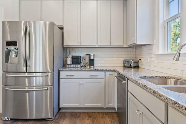 kitchen with dark wood-type flooring, sink, light stone counters, appliances with stainless steel finishes, and white cabinetry