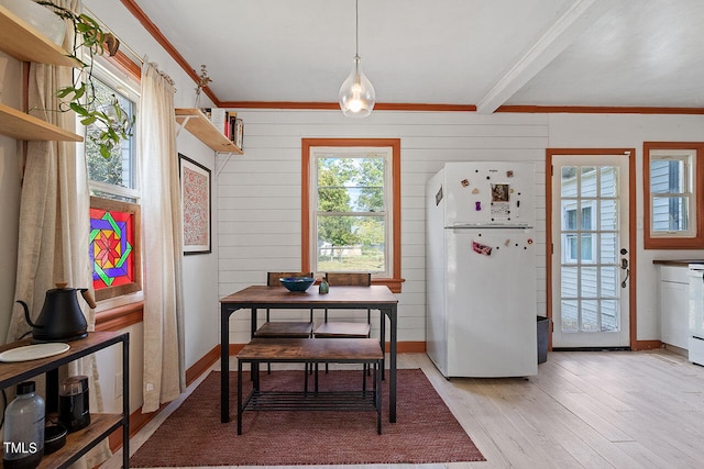 dining space with light hardwood / wood-style floors, a healthy amount of sunlight, beamed ceiling, and wood walls