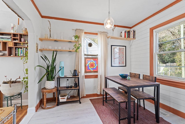 dining room with crown molding, wooden walls, wood-type flooring, and a wealth of natural light