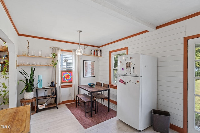 dining room featuring beam ceiling, ornamental molding, a wealth of natural light, and light wood-type flooring