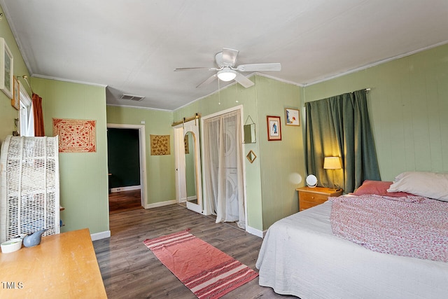 bedroom featuring ceiling fan, ornamental molding, dark hardwood / wood-style flooring, and a barn door