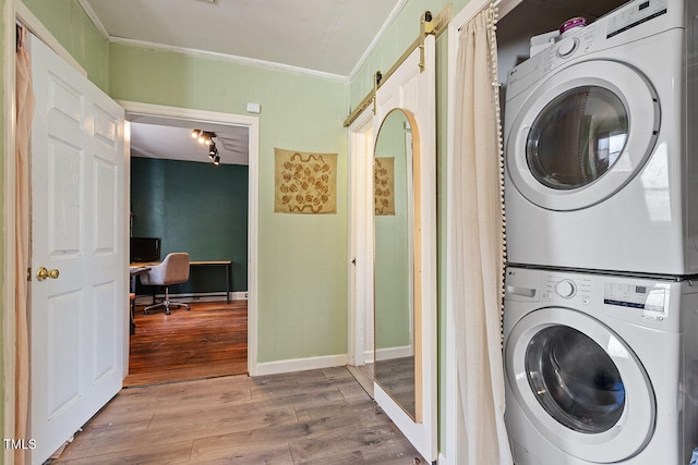 laundry room with stacked washer / dryer, crown molding, wood-type flooring, and a barn door