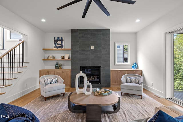 living room with a ceiling fan, wood finished floors, baseboards, stairway, and a tile fireplace