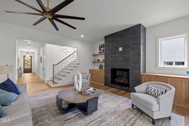 living room with light wood-type flooring, a fireplace, recessed lighting, ceiling fan, and stairs