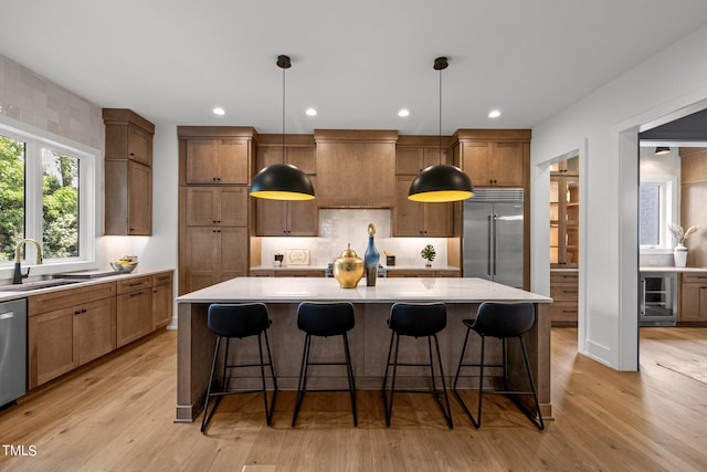 kitchen with light wood-type flooring, decorative light fixtures, sink, stainless steel appliances, and a spacious island