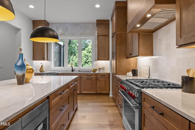 kitchen featuring stainless steel appliances, custom exhaust hood, light wood finished floors, brown cabinetry, and recessed lighting