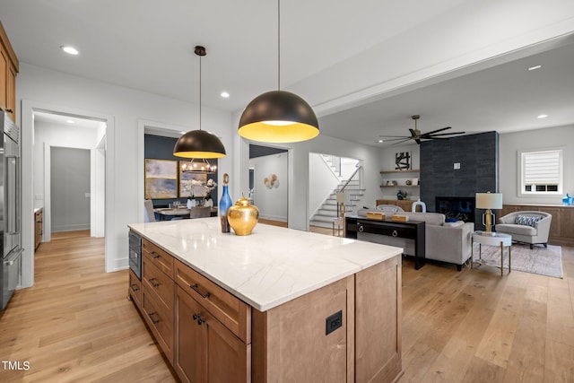 kitchen featuring light wood-type flooring, a tile fireplace, pendant lighting, a kitchen island, and light stone countertops