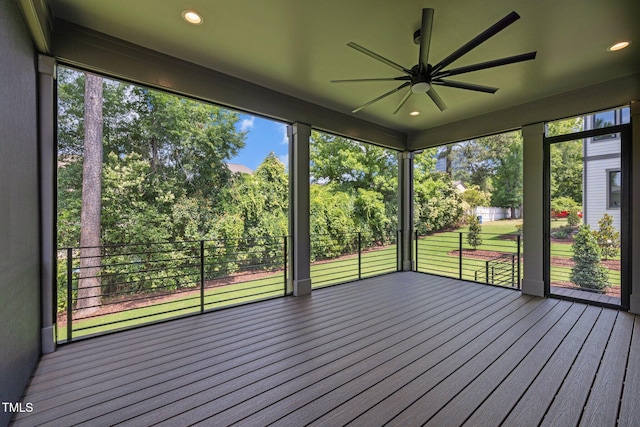 unfurnished sunroom with ceiling fan, plenty of natural light, and view of wooded area