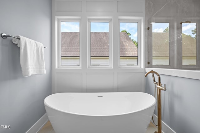 bathroom featuring healthy amount of natural light, baseboards, and a freestanding tub
