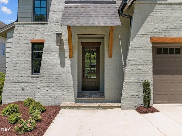 view of exterior entry with an attached garage and brick siding