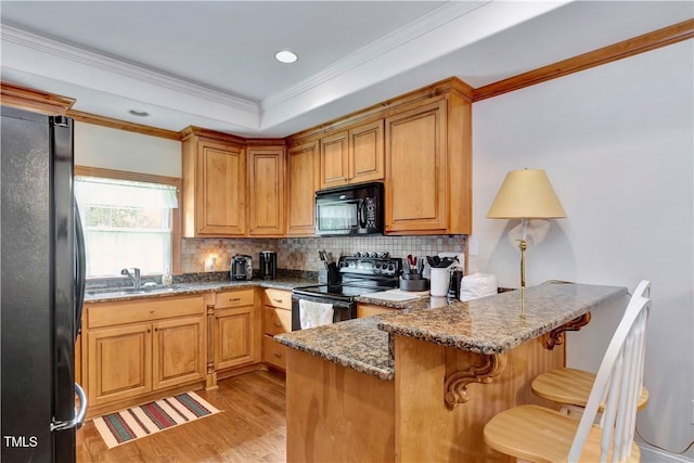 kitchen featuring light stone countertops, sink, black appliances, kitchen peninsula, and a breakfast bar area