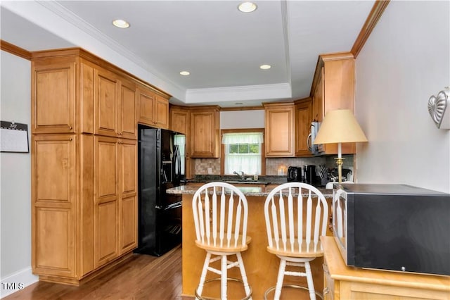 kitchen featuring tasteful backsplash, black refrigerator with ice dispenser, light hardwood / wood-style floors, dark stone counters, and a breakfast bar area