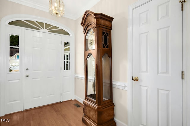 foyer with a notable chandelier, ornamental molding, and wood-type flooring