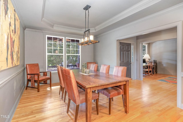 dining area with ornamental molding, a tray ceiling, and light wood-type flooring