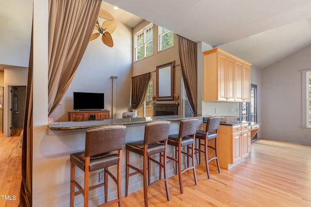 kitchen with light hardwood / wood-style floors, a breakfast bar, kitchen peninsula, and light brown cabinets