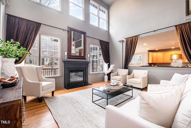 living room with a towering ceiling, a fireplace with flush hearth, a wealth of natural light, and light wood-style floors