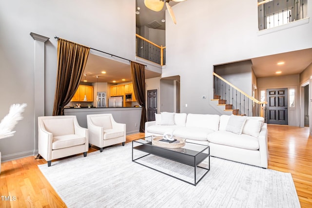 living room with light wood-type flooring, stairs, baseboards, and a towering ceiling