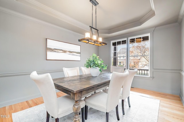 dining space featuring baseboards, ornamental molding, a raised ceiling, and light wood-style floors