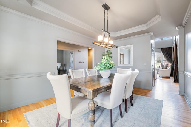 dining area featuring light wood-style flooring, ornamental molding, a raised ceiling, and baseboards