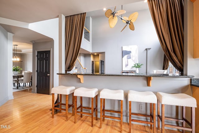 kitchen with light wood-style floors, a breakfast bar, dark stone countertops, and an inviting chandelier