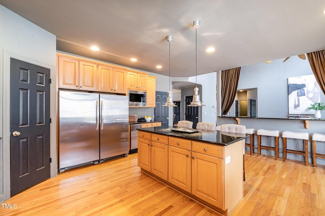 kitchen featuring light brown cabinets, light wood-style flooring, a kitchen island, appliances with stainless steel finishes, and pendant lighting