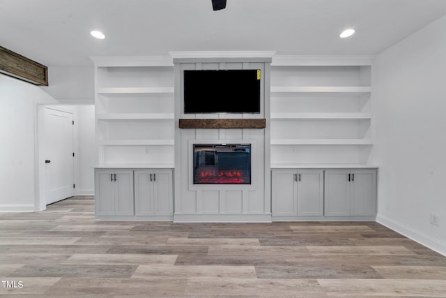 unfurnished living room featuring a large fireplace, light wood-type flooring, and built in features