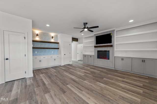 unfurnished living room with a fireplace, wood-type flooring, built in features, and ceiling fan