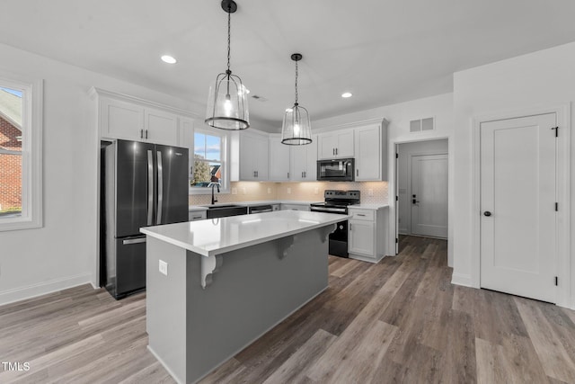 kitchen with light hardwood / wood-style flooring, sink, black appliances, a center island, and white cabinets