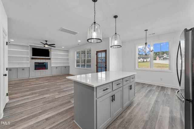 kitchen featuring a kitchen island, hanging light fixtures, ceiling fan, stainless steel refrigerator, and light hardwood / wood-style flooring