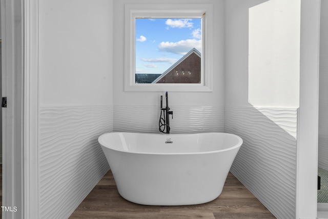 bathroom featuring tile walls, hardwood / wood-style floors, and a tub to relax in