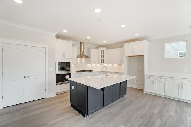 kitchen featuring white cabinetry, wall chimney range hood, stainless steel oven, and a kitchen island with sink