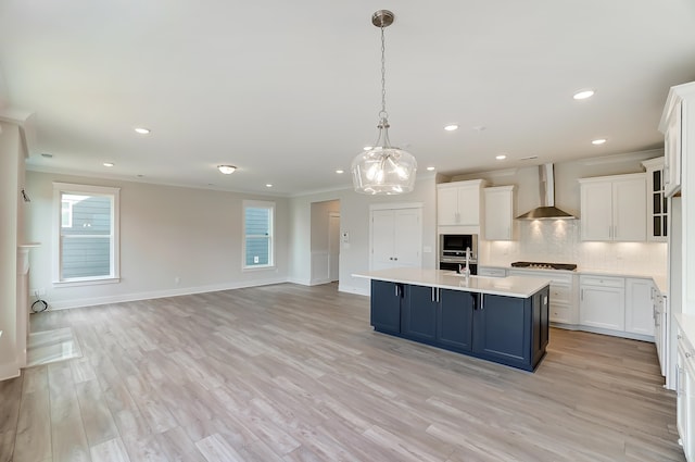 kitchen featuring wall chimney exhaust hood, pendant lighting, white cabinets, blue cabinetry, and light hardwood / wood-style flooring