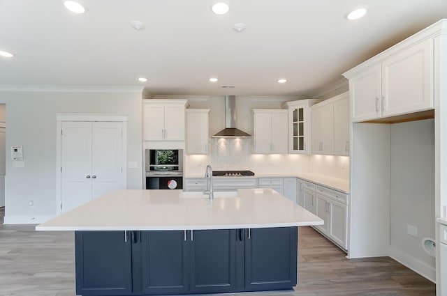 kitchen with wall chimney range hood, a breakfast bar area, white cabinetry, a kitchen island with sink, and light wood-type flooring