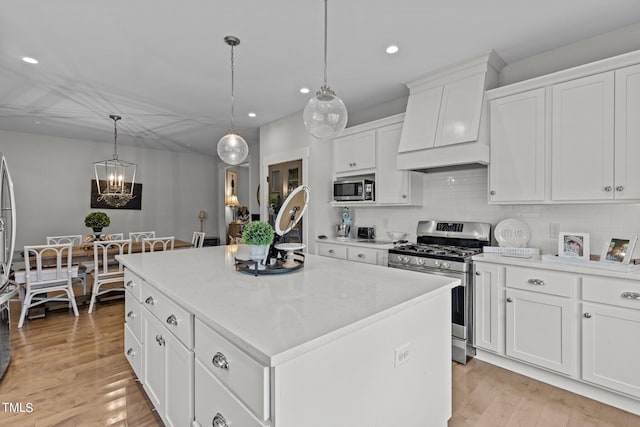 kitchen with pendant lighting, stainless steel appliances, premium range hood, and a kitchen island