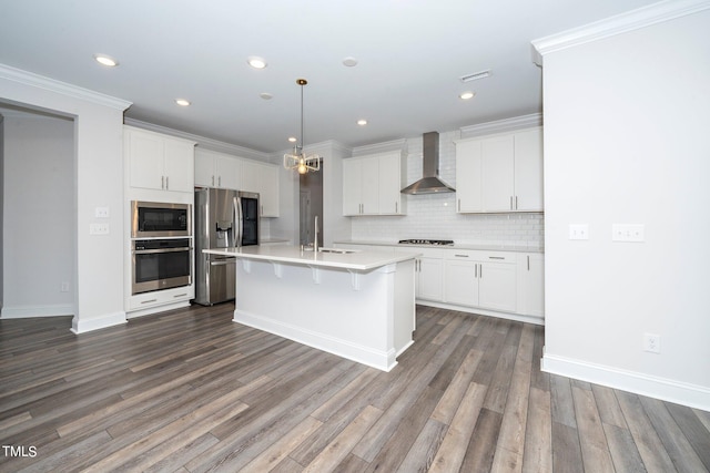 kitchen featuring wall chimney exhaust hood, a kitchen island with sink, hardwood / wood-style floors, appliances with stainless steel finishes, and white cabinetry