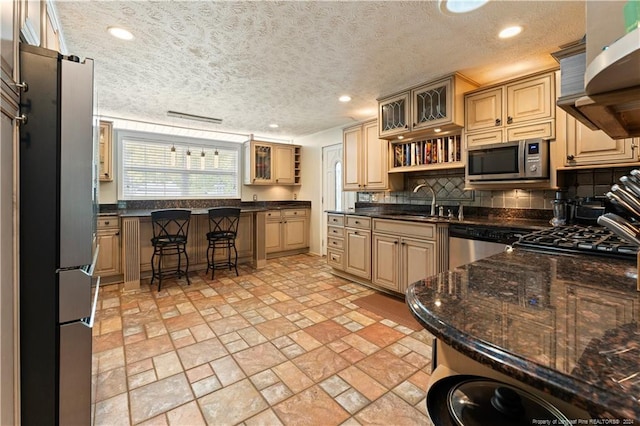 kitchen featuring dark stone counters, range hood, decorative backsplash, appliances with stainless steel finishes, and a textured ceiling