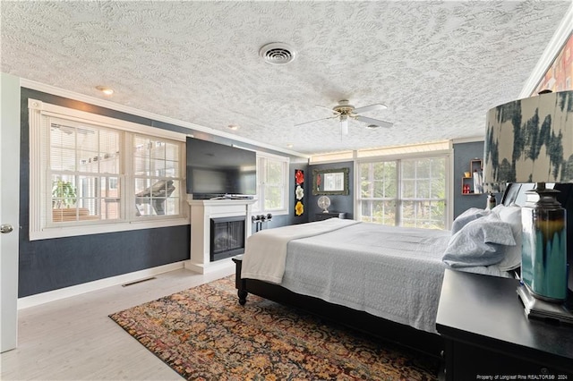 bedroom with ceiling fan, a textured ceiling, light wood-type flooring, and ornamental molding