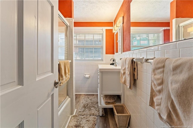 bathroom with combined bath / shower with glass door, hardwood / wood-style floors, tile walls, vanity, and a textured ceiling