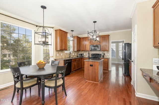 kitchen with a center island, black appliances, hanging light fixtures, and plenty of natural light