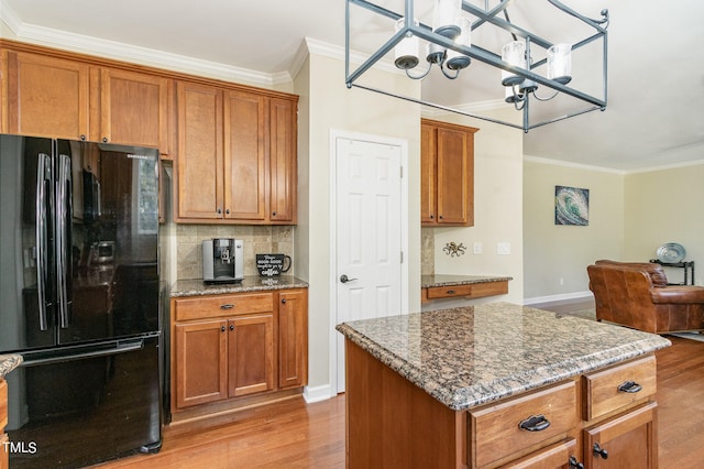 kitchen featuring dark stone countertops, light hardwood / wood-style floors, a center island, and black fridge