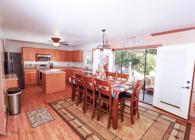 dining space featuring light wood-type flooring, ceiling fan with notable chandelier, and sink