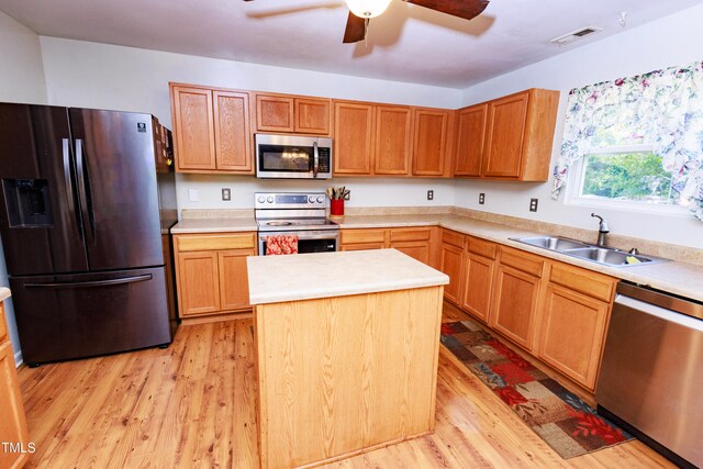 kitchen featuring appliances with stainless steel finishes, a kitchen island, sink, ceiling fan, and light hardwood / wood-style flooring