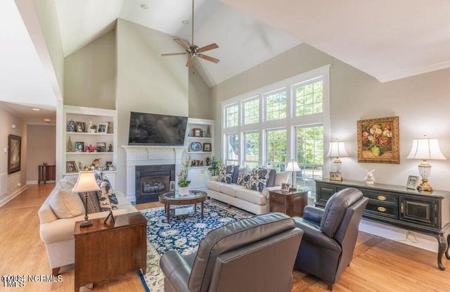 living room with built in features, light hardwood / wood-style floors, ceiling fan, crown molding, and high vaulted ceiling