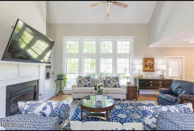 living room featuring a towering ceiling, ceiling fan, a fireplace, and wood finished floors